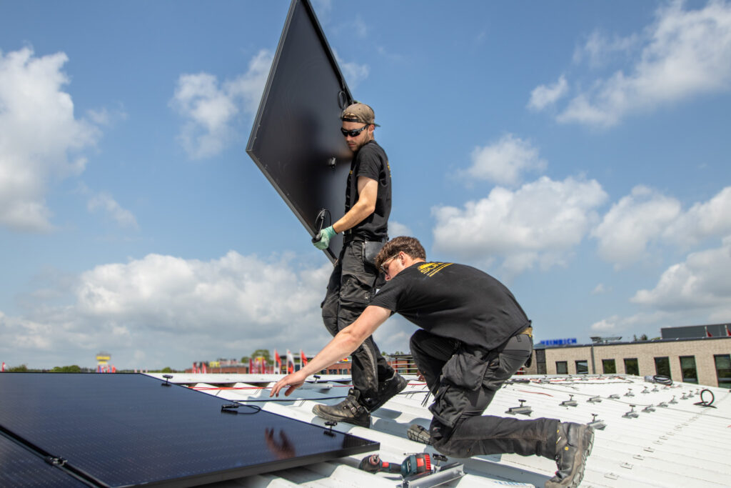 Zwei Monteure von Nordic Sunpower auf einem Hausdach, einer trägt ein Solarmodul.