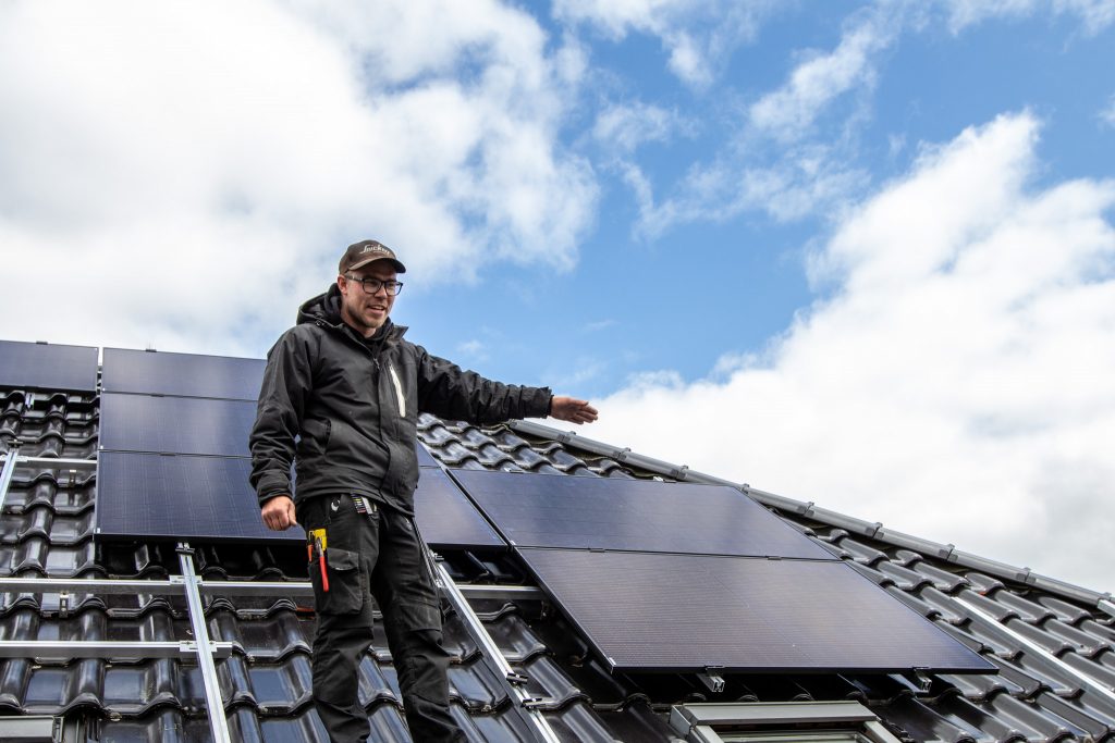 Ein Monteur von Nordic Sunpower steht auf einem Hausdach und zeigt auf bereits installierte Solarpaneele.